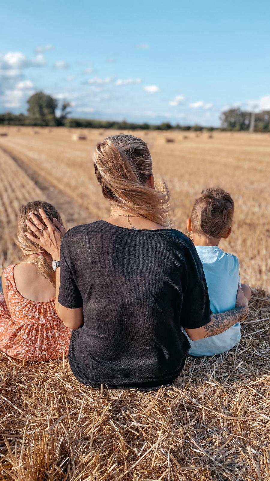 Jessica mit ihren beiden Kindern von hinten auf einem Strohballen im Feld